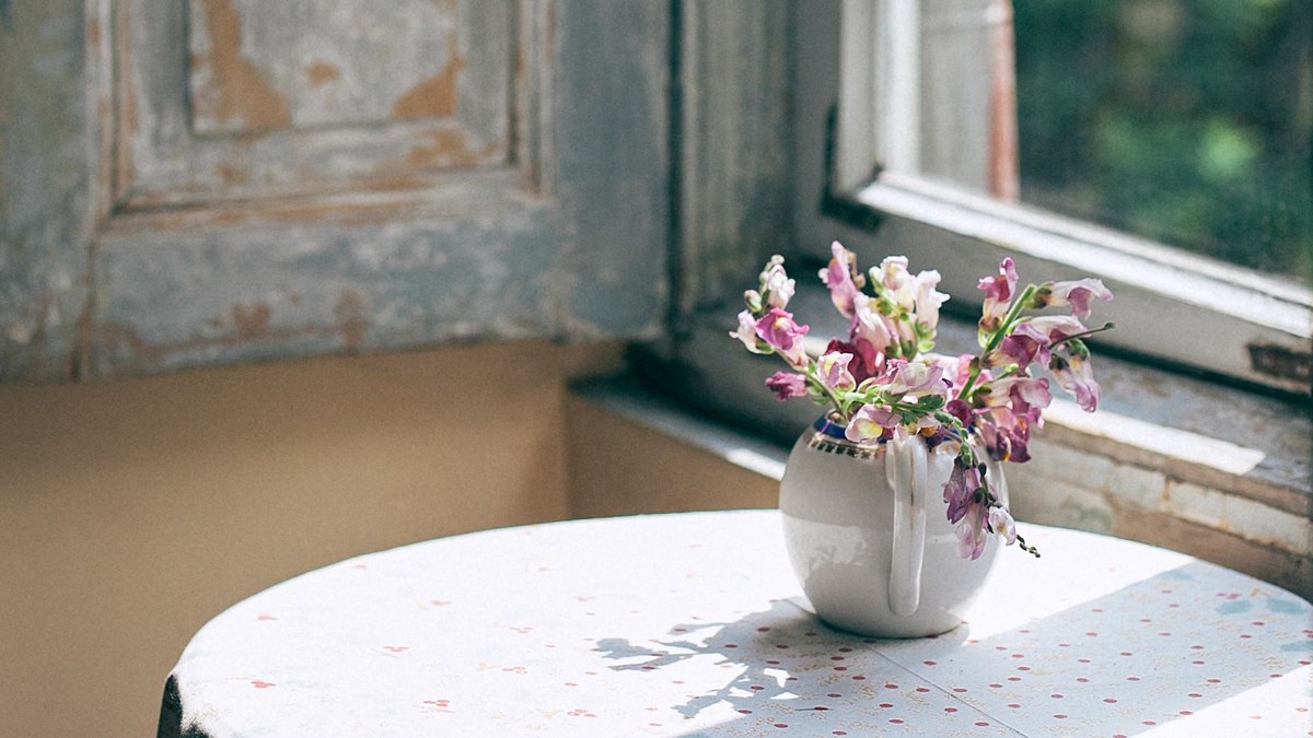 Small pink bouquet in a white jug on a table beside a window