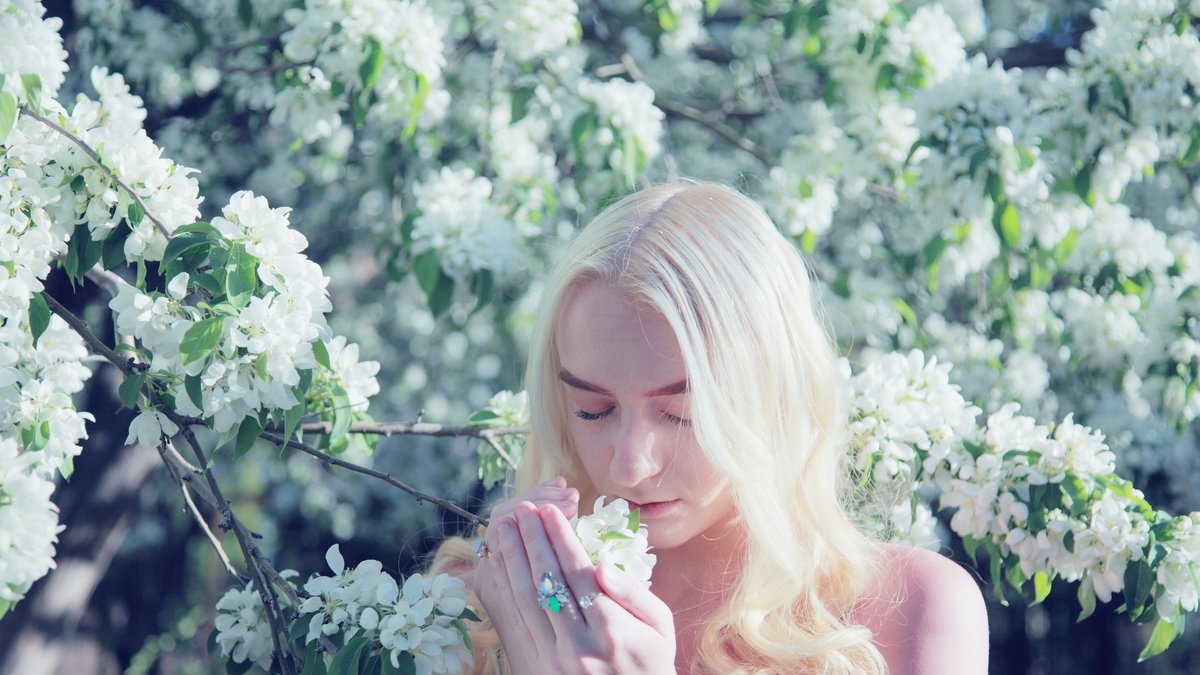 Woman holding a cluster of white blossoms to her nose among flowering branches